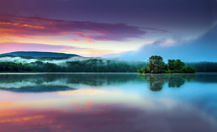 Lake with island and misty mountains at sunrise