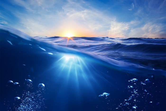 Split view of ocean surface and underwater with sun rays and bubbles
