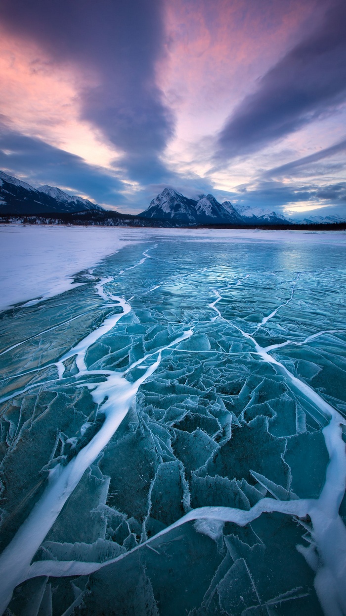 Cracked ice on a frozen lake with mountains and sunset sky