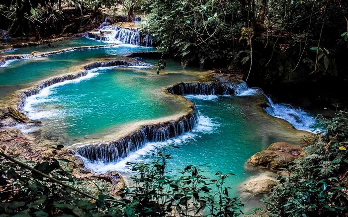 Turquoise waterfalls cascading over limestone terraces in Laos