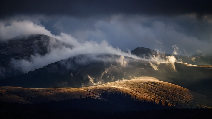 Misty mountains with sunlight breaking through clouds in Romania