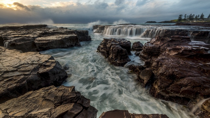 Ocean waves crashing over rocks with a waterfall