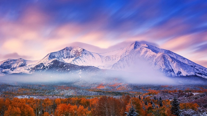 Snowy mountain peaks at sunset with autumn forest
