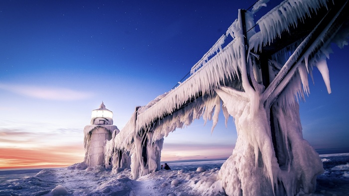 Frozen lighthouse and pier covered in ice at sunset