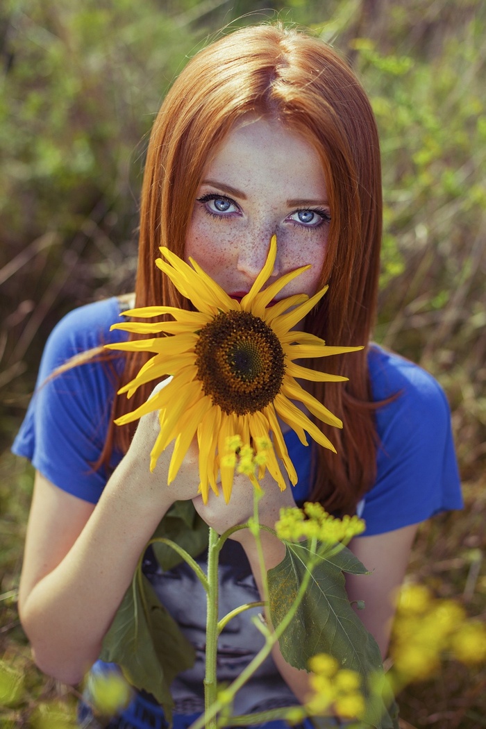 Redhead woman with blue eyes holding a sunflower