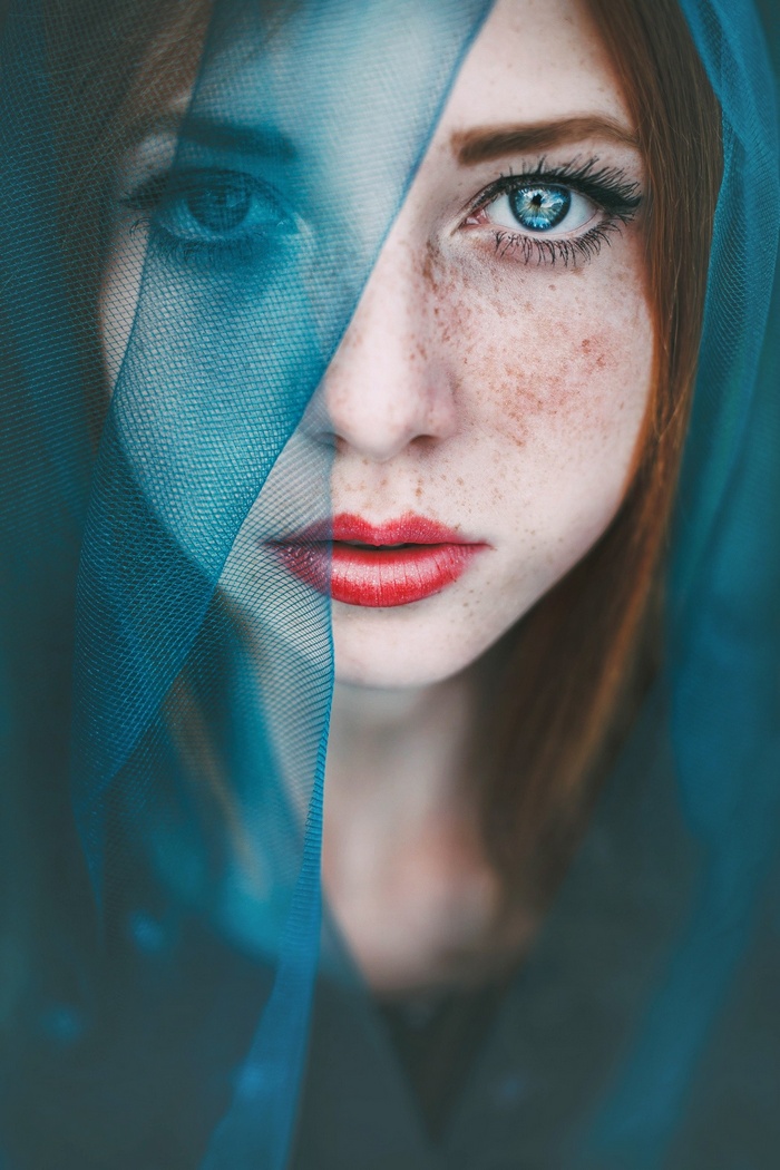 Woman with red hair and blue eyes behind a blue veil