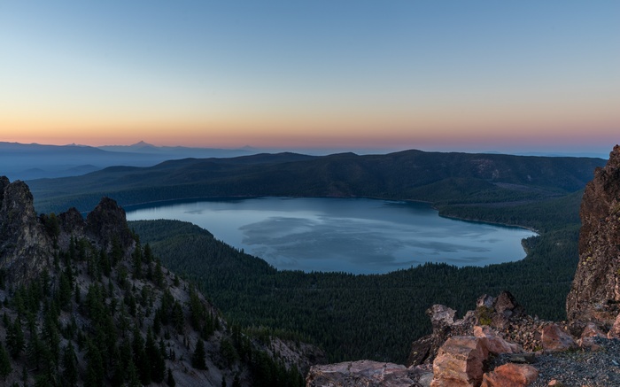 Lake surrounded by forest at sunrise with distant mountains