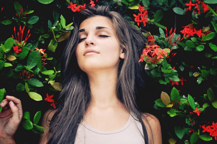 Woman with eyes closed among red flowers and green leaves