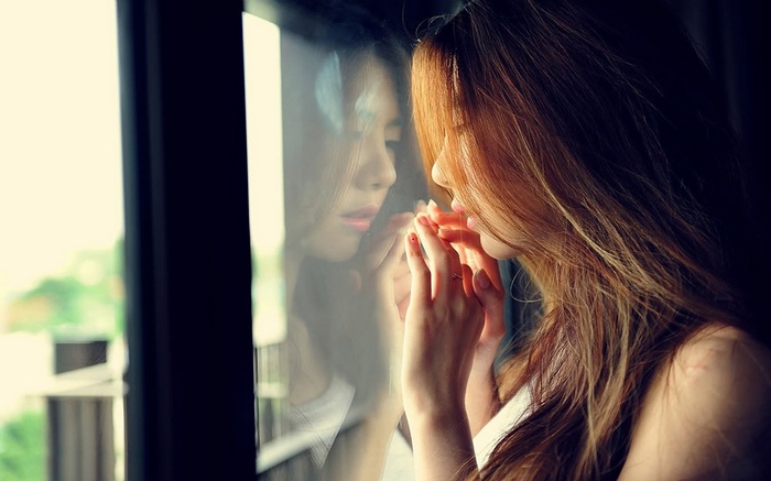 Asian woman looking at her reflection in glass
