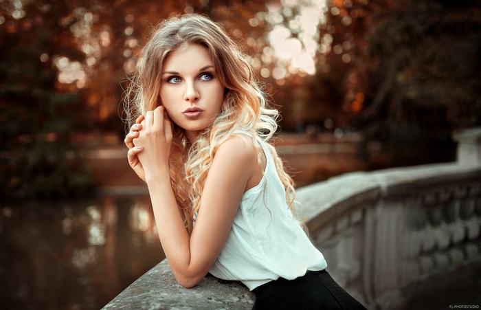 Woman with blonde curly hair leaning on a stone railing
