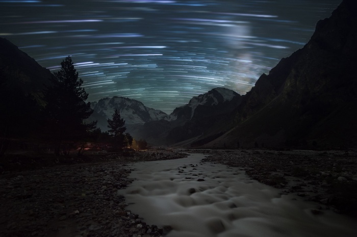 Star trails over a mountain valley with a river