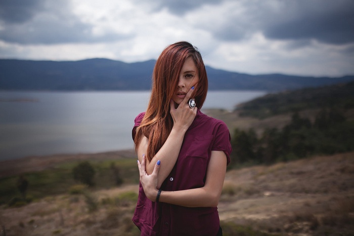 Woman with red hair posing outdoors by a lake