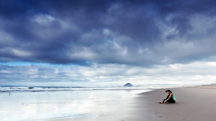 Woman in hat sitting on a beach under stormy clouds