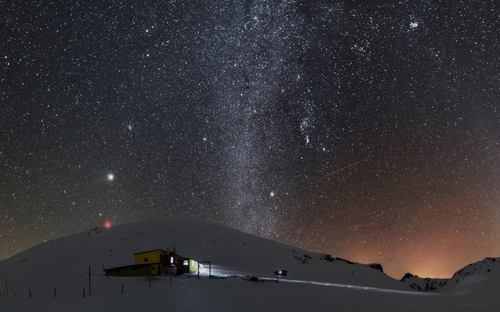 Milky Way over a snowy mountain cabin at night