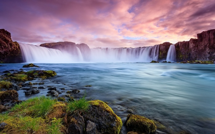 Waterfall cascading over rocks with colorful sky