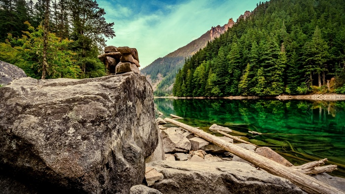 Rocky shore of a clear green lake with a forest and mountain backdrop