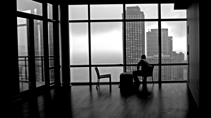 Man sitting in a modern apartment overlooking a city skyline