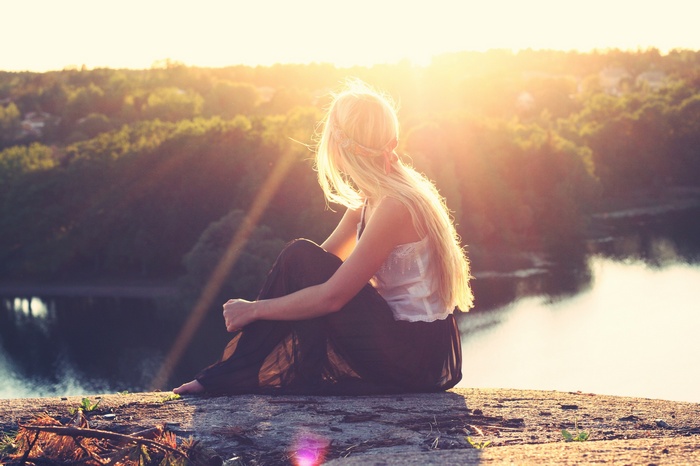 Woman with long blonde hair sitting by a lake at sunset