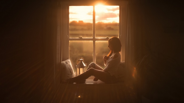 Woman sitting by the window at sunset