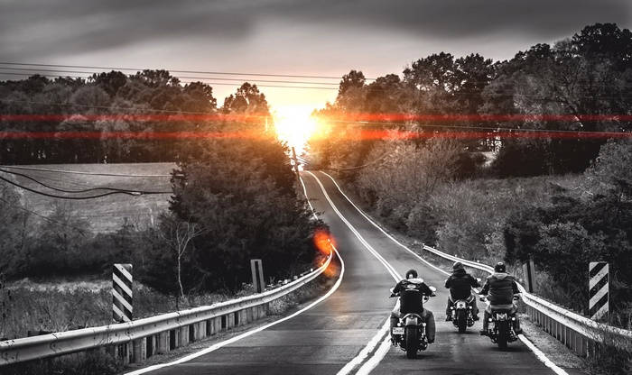 Motorcyclists ride on a road at sunset