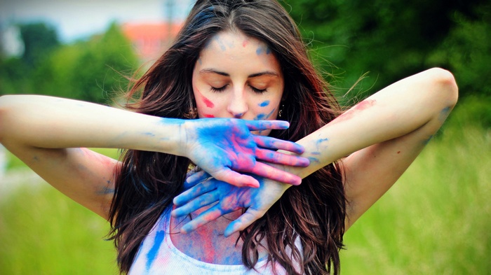 Woman covered in colorful paint with hands in front of face