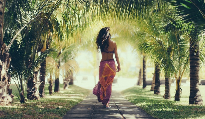 Woman walking on a path lined with palm trees