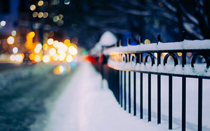 Snowy street with bokeh lights and a fence