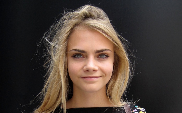 Cara Delevingne smiling against a black background