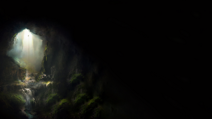 Person rappelling into a dark cave with waterfalls