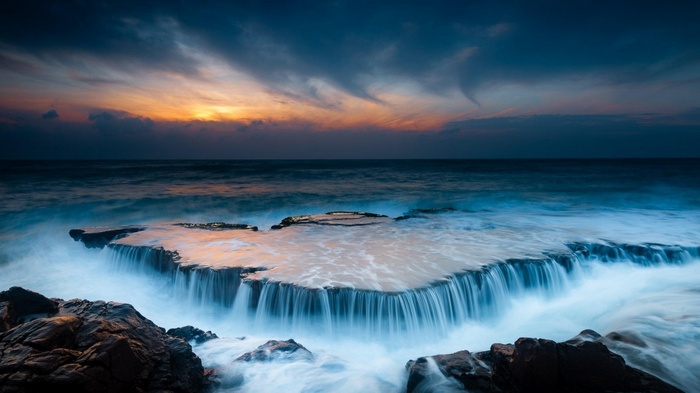 Ocean waves crashing over rocks at sunset