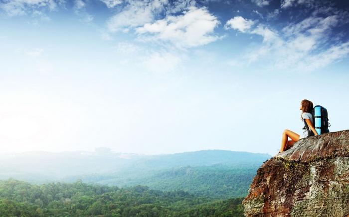 Woman with backpack sitting on a cliff overlooking a forest