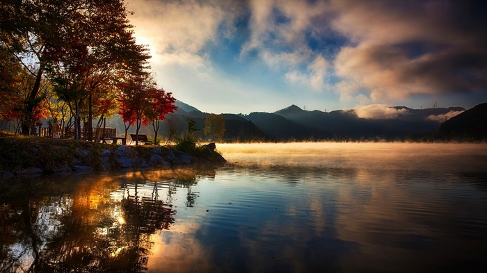 Misty lake with autumn trees and mountains at sunrise
