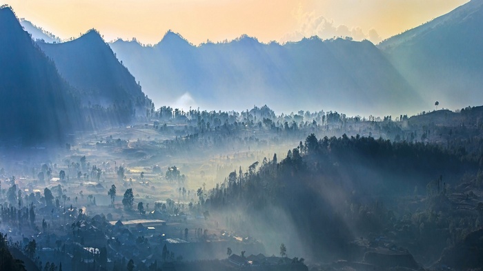 Misty valley with sun rays over Indonesian mountains