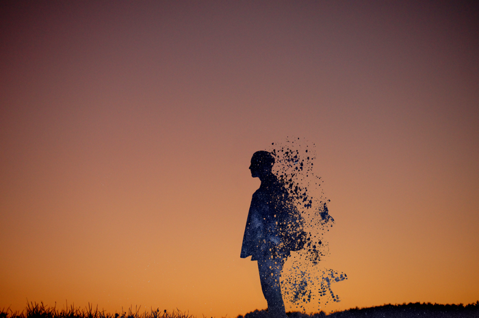 Silhouette of a person dissolving into galaxy dust at sunset