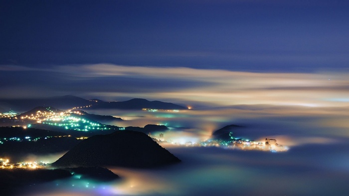 City lights in the mist over mountains at night