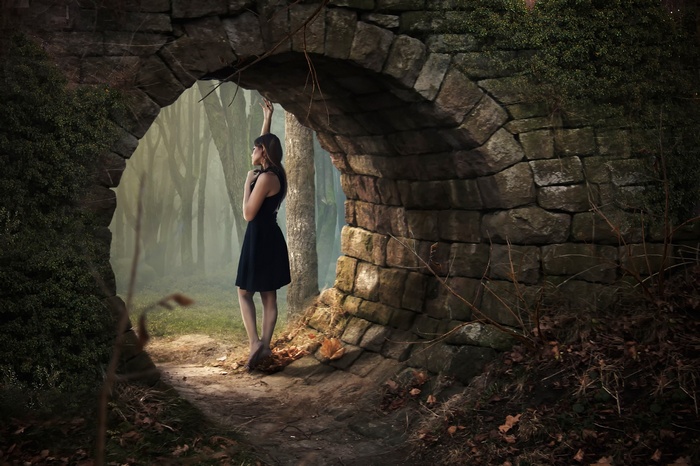 Woman in black dress under stone archway in forest