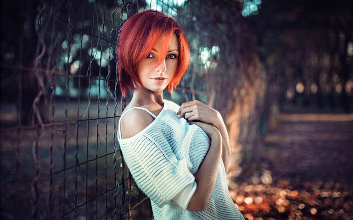 Redhead woman in white clothing leaning on fence