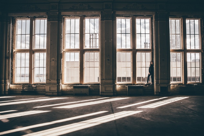 Woman standing by large windows with light and shadows
