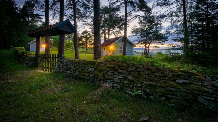 Stone wall and gate leading to houses by a lake at sunset