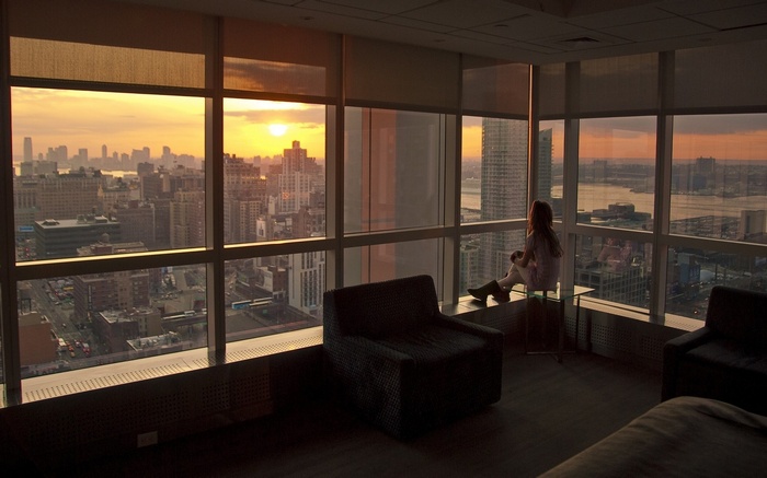 Woman looking at city skyline at sunset from interior room