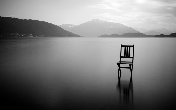 A lone chair in a calm lake with mountains