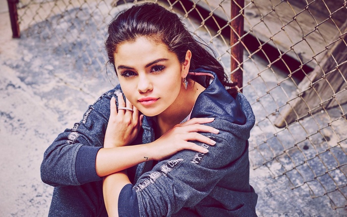 Selena Gomez sitting by a chain-link fence