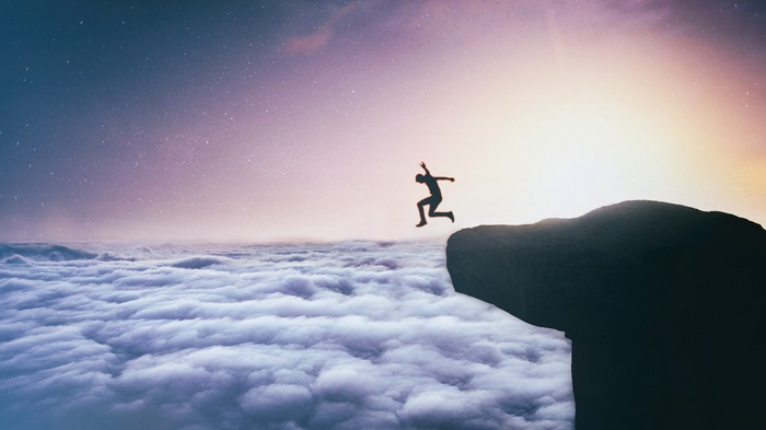 Silhouette of a person jumping off a cliff into clouds