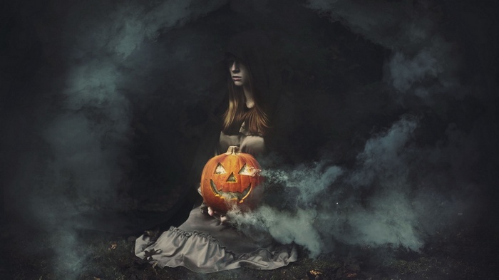 Woman in dark smoke holding a jack-o'-lantern