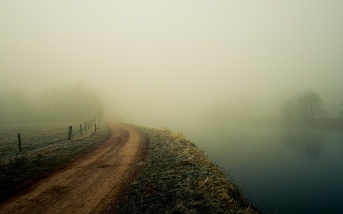 Dirt road by a misty river with a fence