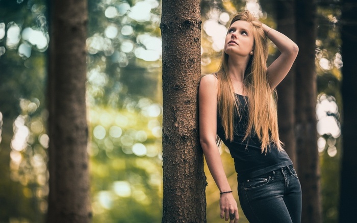 Woman with long blonde hair leaning against a tree in a forest