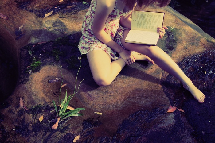 Woman reading a book on a rock by the water