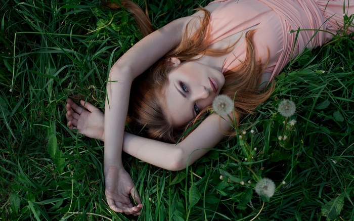 Redhead woman lying in green grass with dandelions