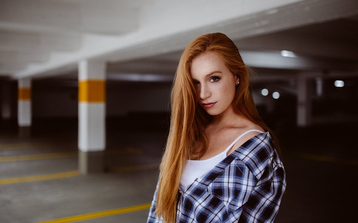 Redhead woman with freckles in a plaid shirt in a garage