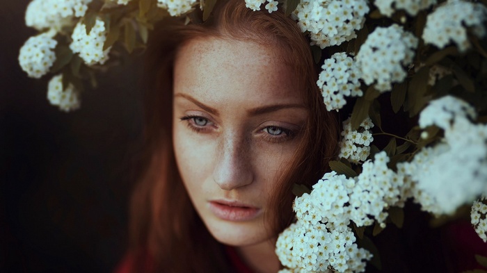 Woman with red hair and freckles surrounded by white flowers